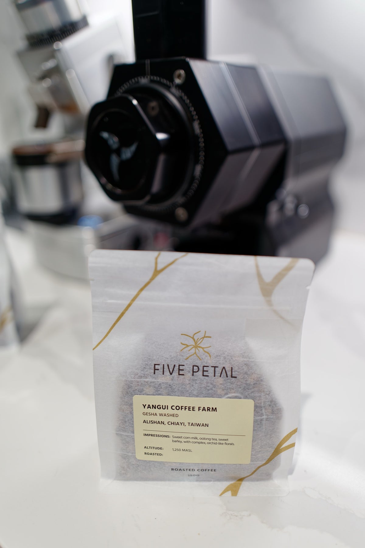 150g bag of Yangui Coffee Farm Gesha Washed coffee standing in front of a black coffee grinder.